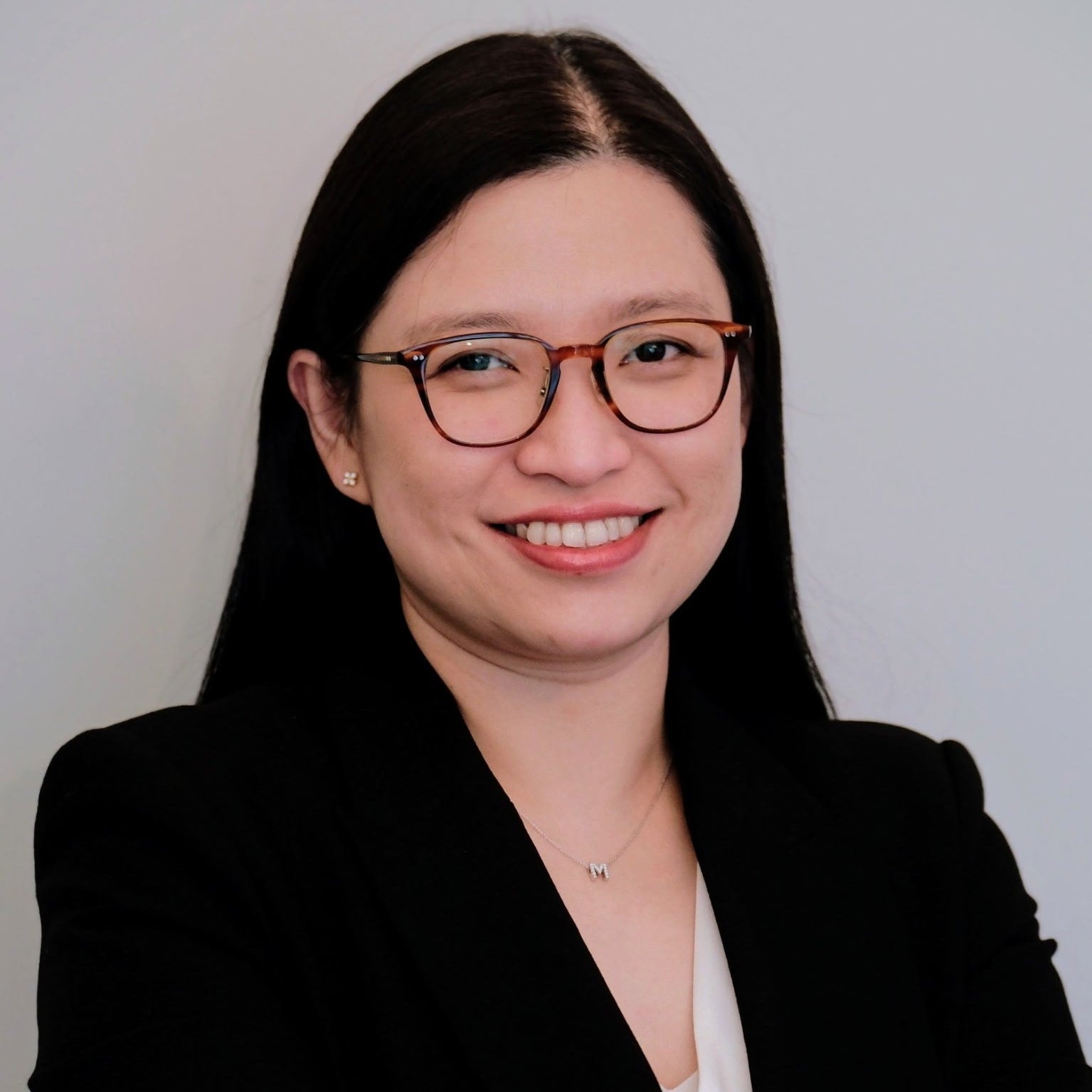 Woman wearing glasses and a black blazer against a plain background